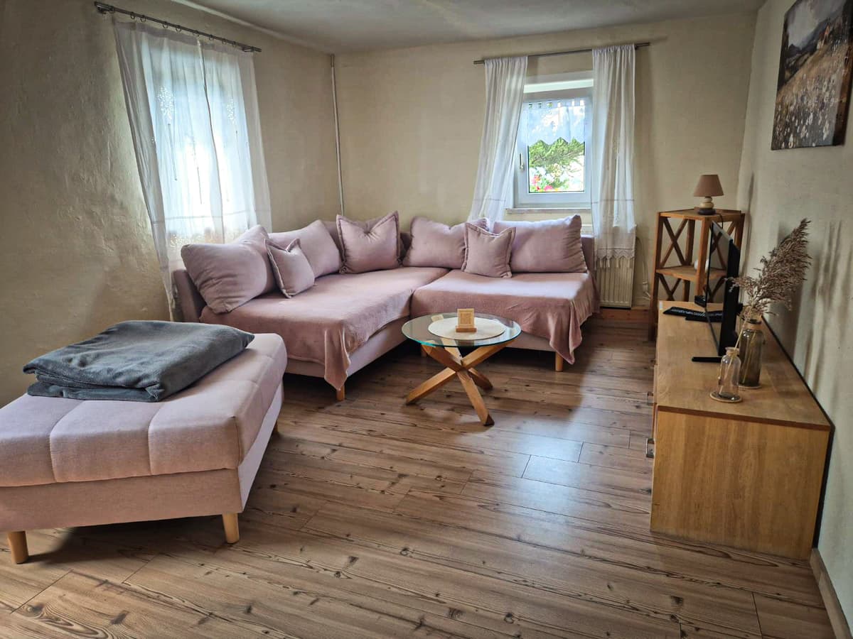 Wohnzimmer der kleinen Ferienwohnung mit Sitzlandschaft und zwei Fenstern